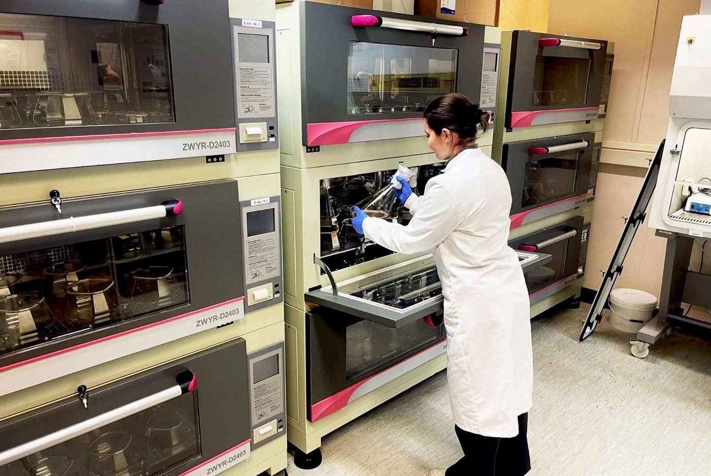 A scientist in a white coat working at a bank of laboratory incubators